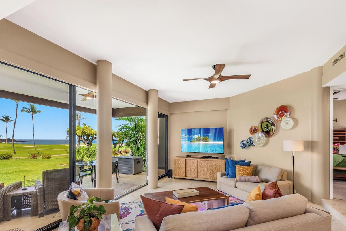 A spacious living area with a large TV, comfortable seating, a ceiling fan, and a view of a golf course.