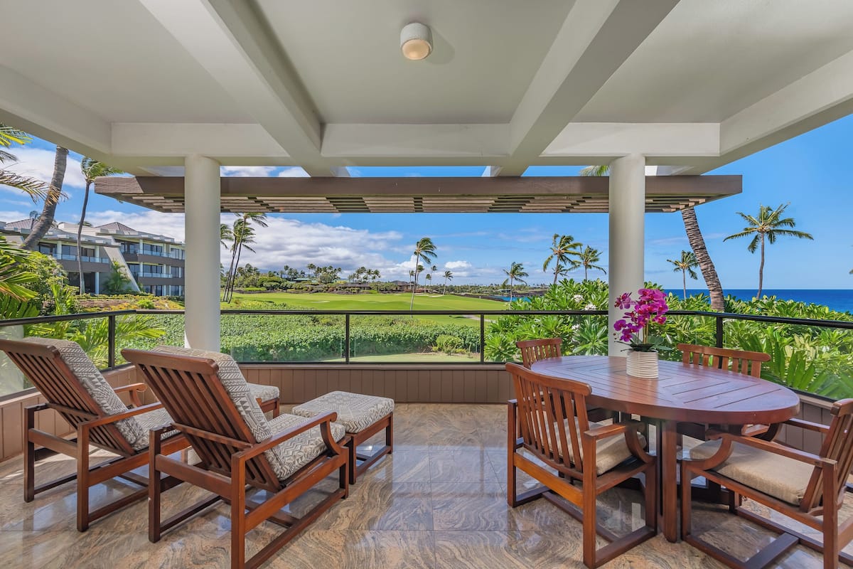 A covered outdoor seating area with a view of a golf course and the ocean.