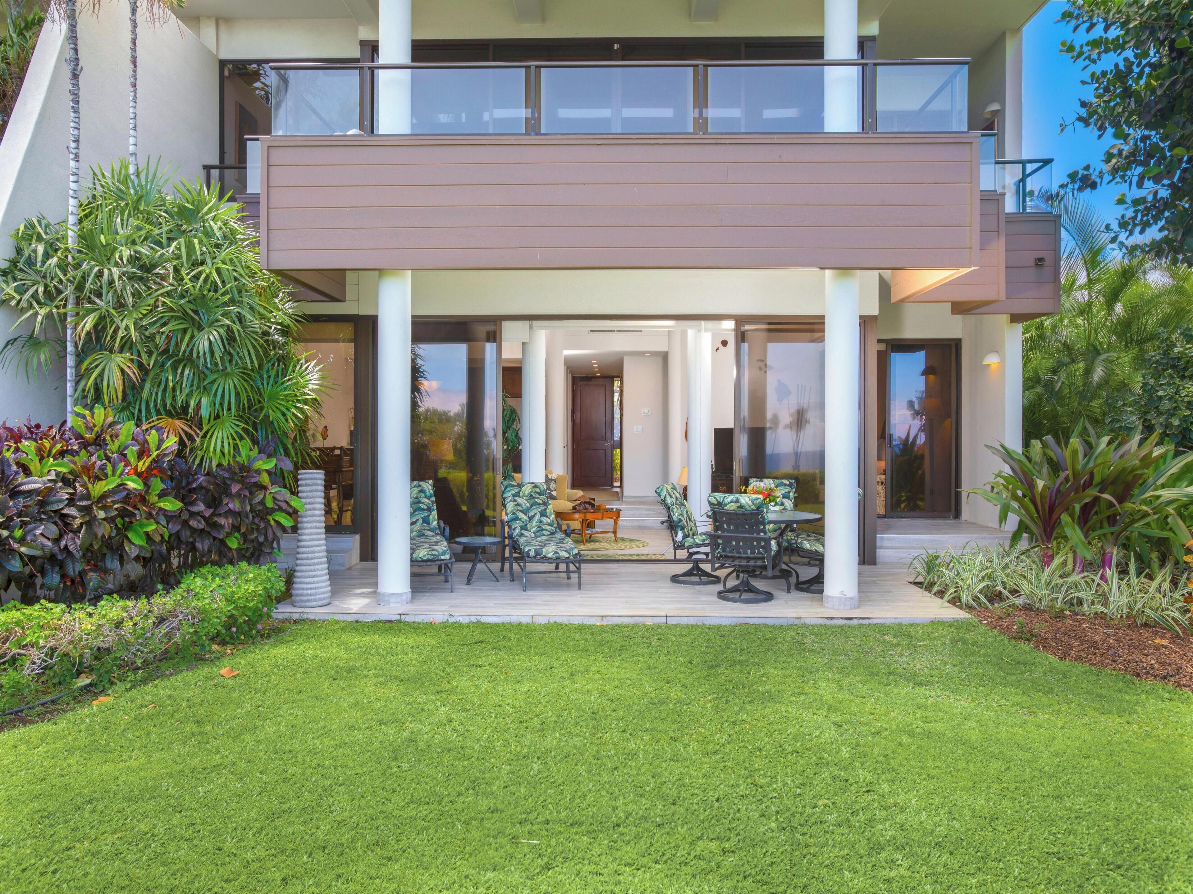 A modern two-story house with a covered patio, outdoor seating, and lush landscaping.
