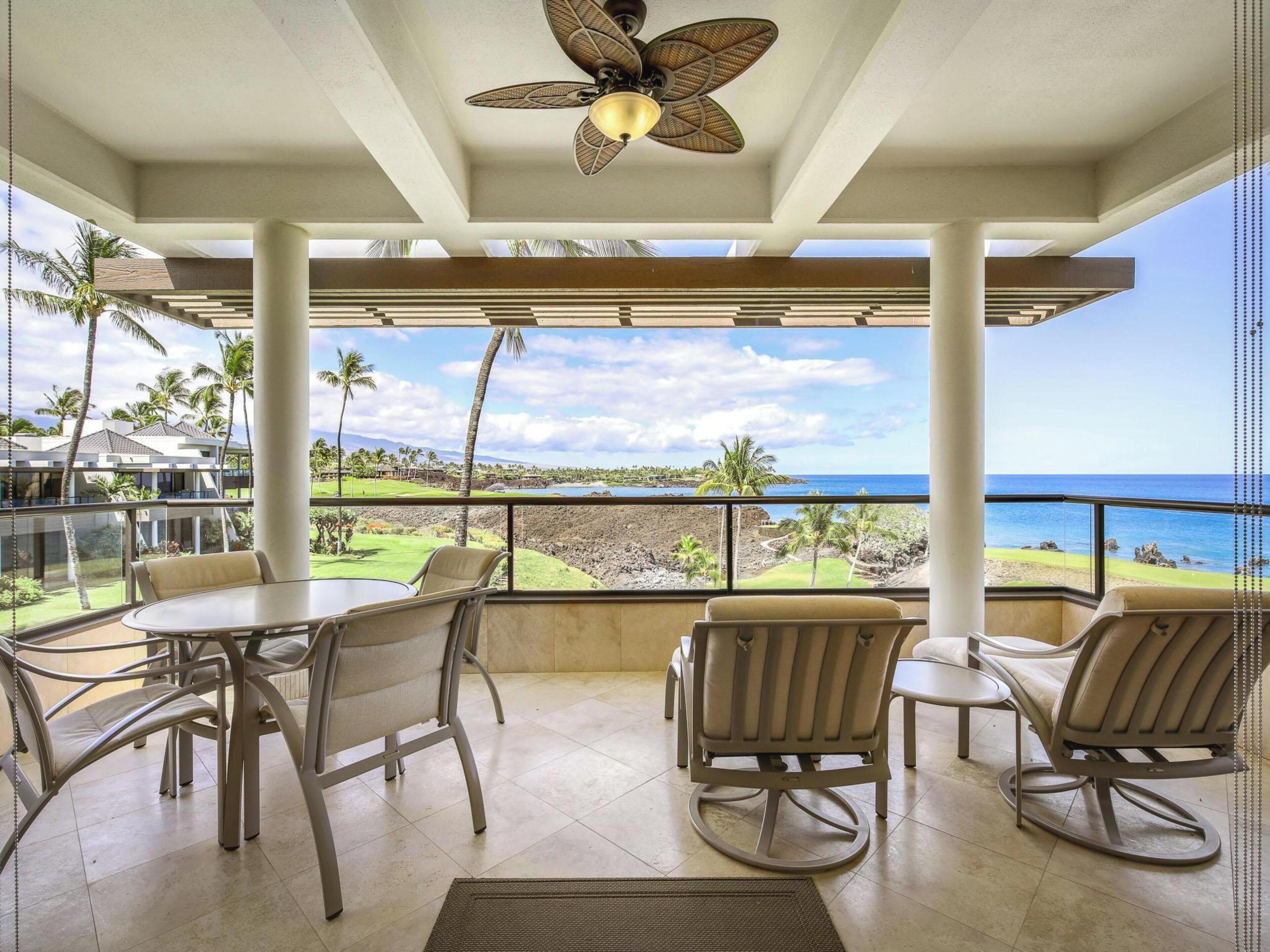 A covered outdoor seating area with a table and chairs, overlooking a scenic view of the ocean and a golf course.