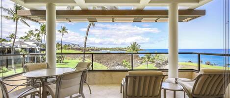 A covered outdoor seating area with a table and chairs, overlooking a scenic view of the ocean and a golf course.
