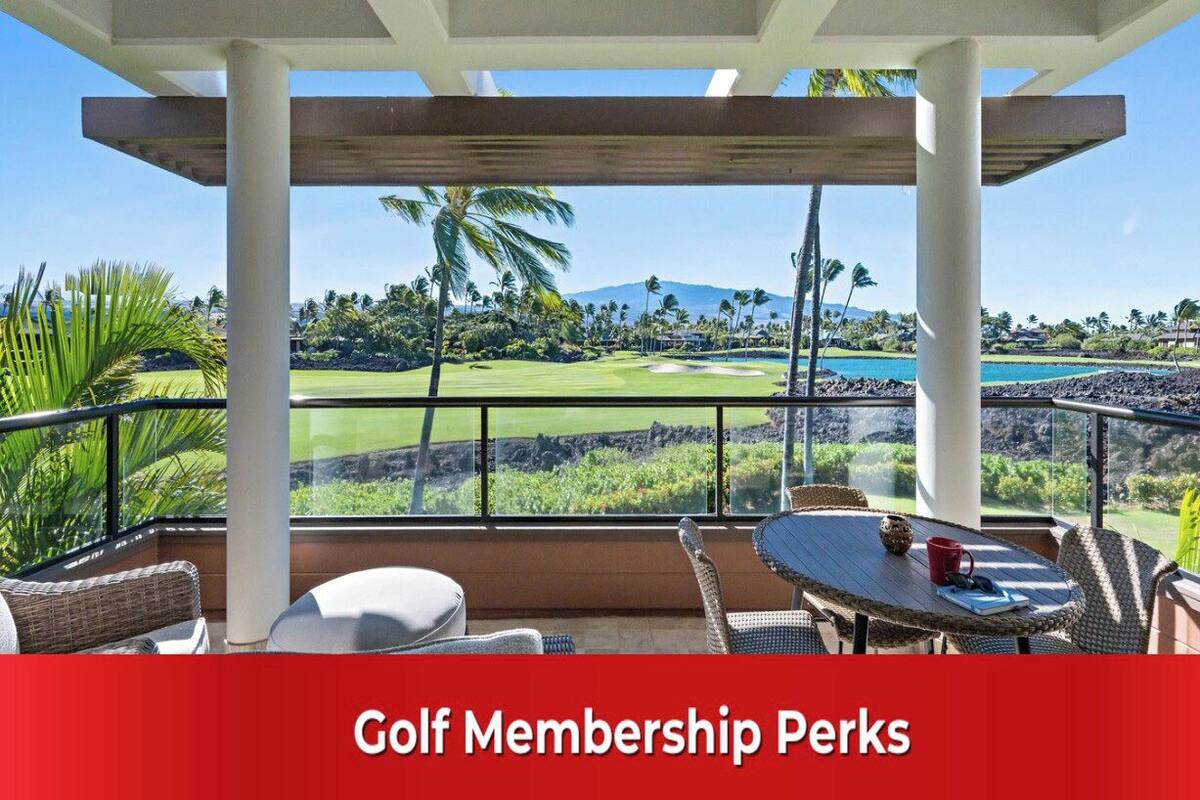 A covered outdoor seating area with a view of a golf course, palm trees, and a mountain in the distance.