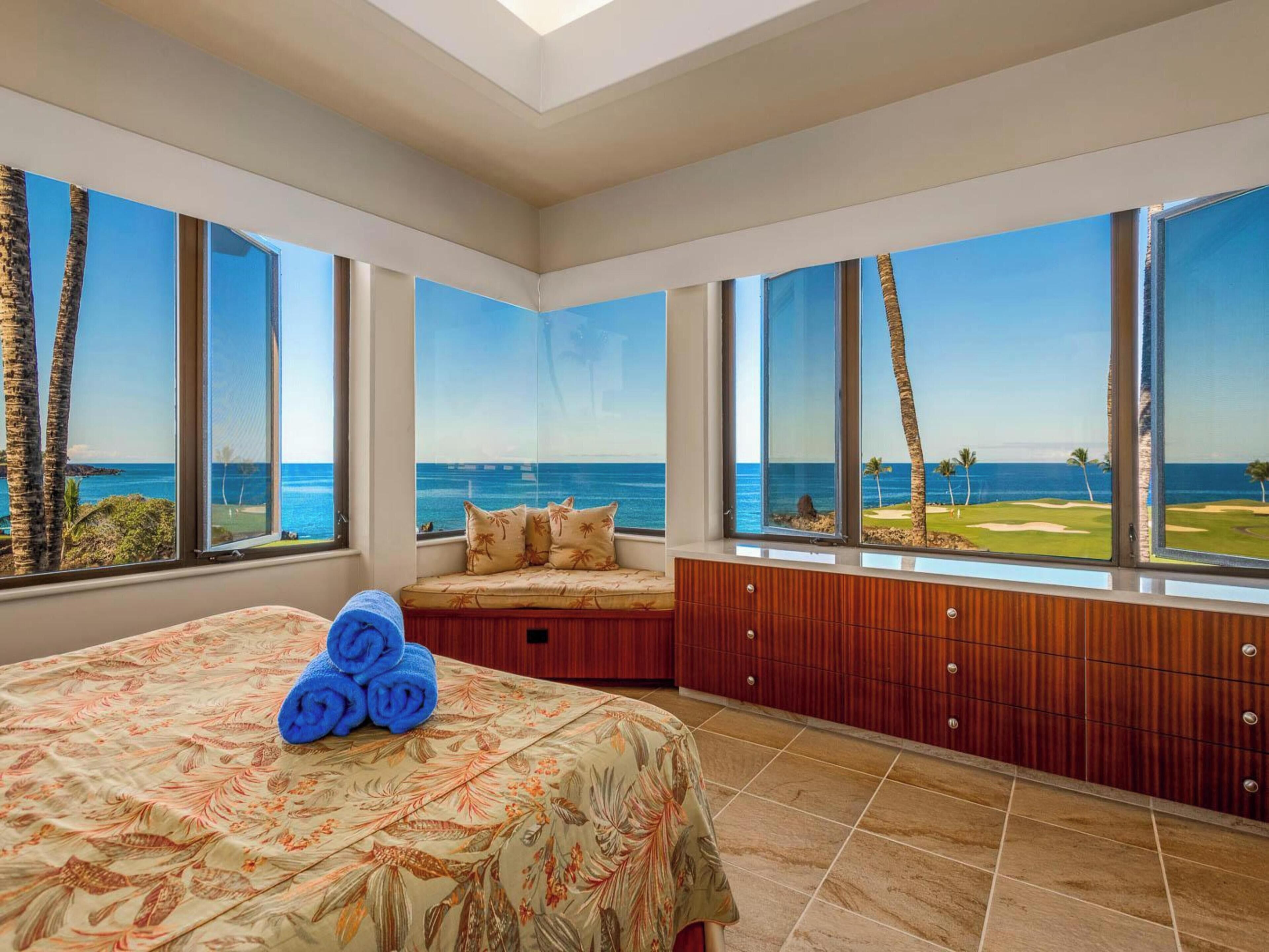 Un dormitorio con una cama grande, una zona de estar con vista al océano y un armario de madera.