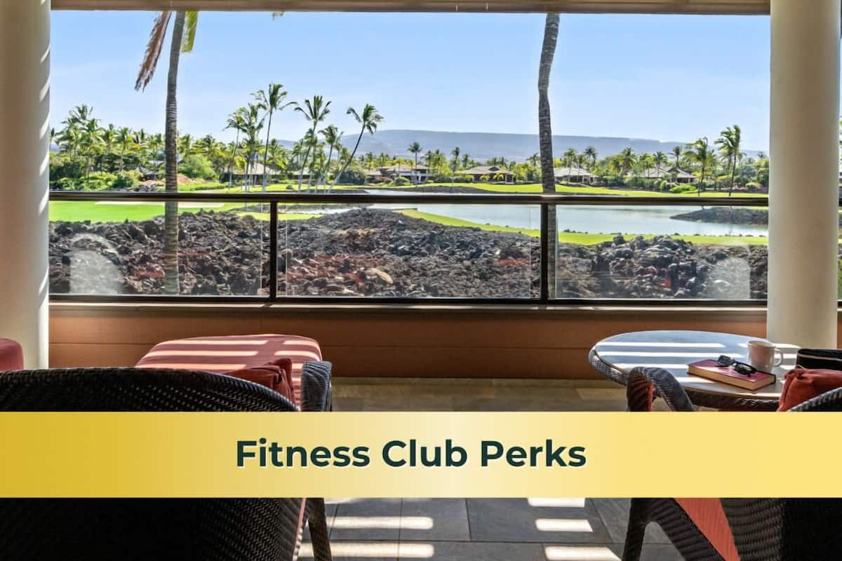 A fitness club with a view of a landscaped area, palm trees, and a body of water.