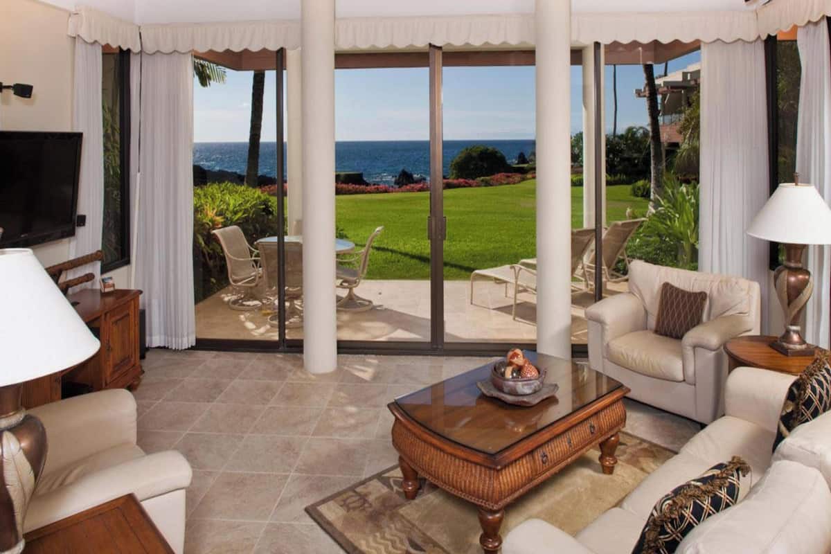A spacious living room with a large sliding glass door leading to a patio with a view of the ocean.