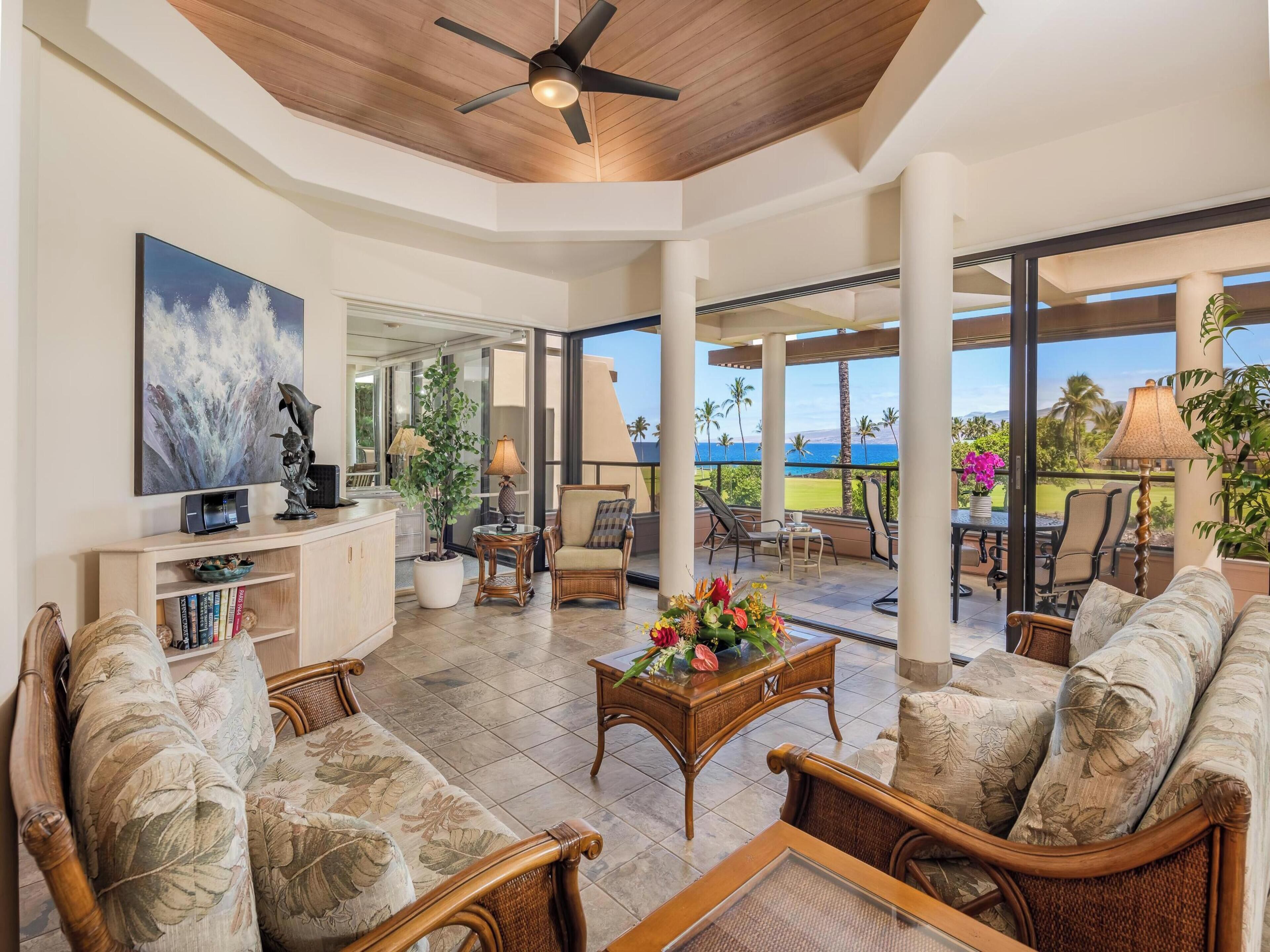 A spacious living area with a ceiling fan, a large painting, and a view of the ocean through large windows.