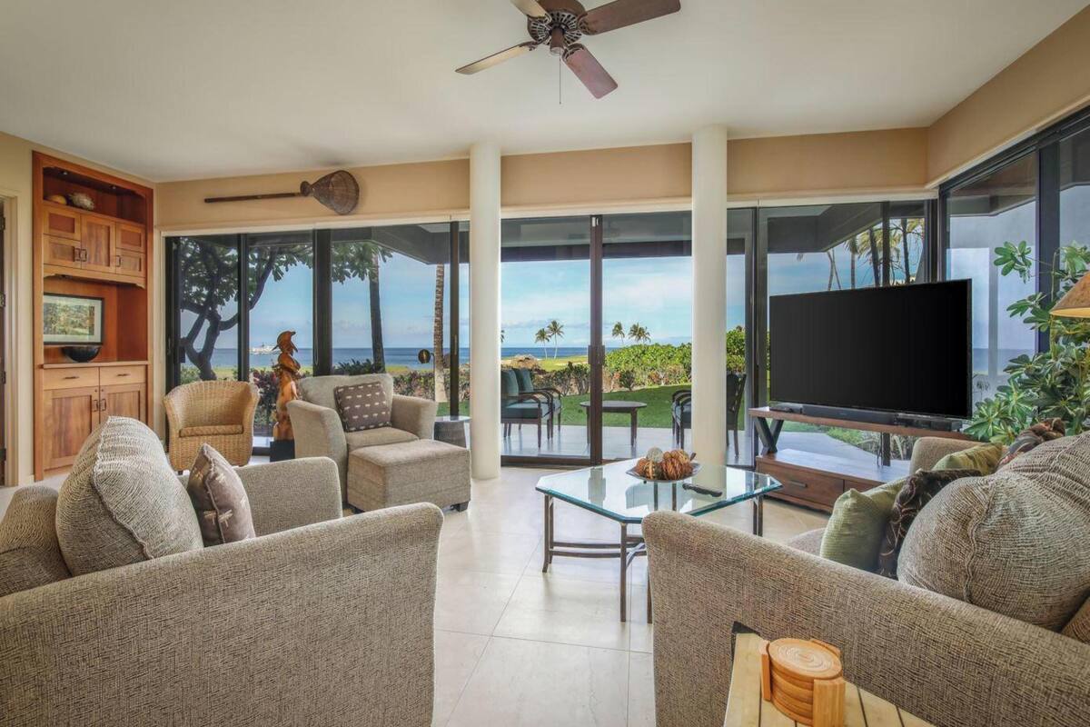 A spacious living room with a large TV, comfortable seating, and a view of the ocean.