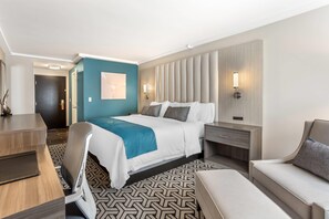 A hotel room with a bed, bedside tables, a desk, a chair, and a sofa.