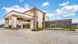 A modern hotel entrance with a prominent sign, a covered entrance area, and landscaped gardens. - The Ashi, an Ascend Collection Hotel (North Brunswick)
