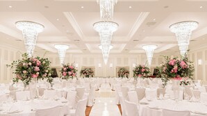 A banquet hall with round tables, white chairs, and large floral centerpieces. - The Ashi, an Ascend Collection Hotel (North Brunswick)