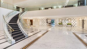 A spacious, multi-level lobby with a grand staircase, polished marble floors, and modern lighting fixtures. - The Ashi, an Ascend Collection Hotel (North Brunswick)