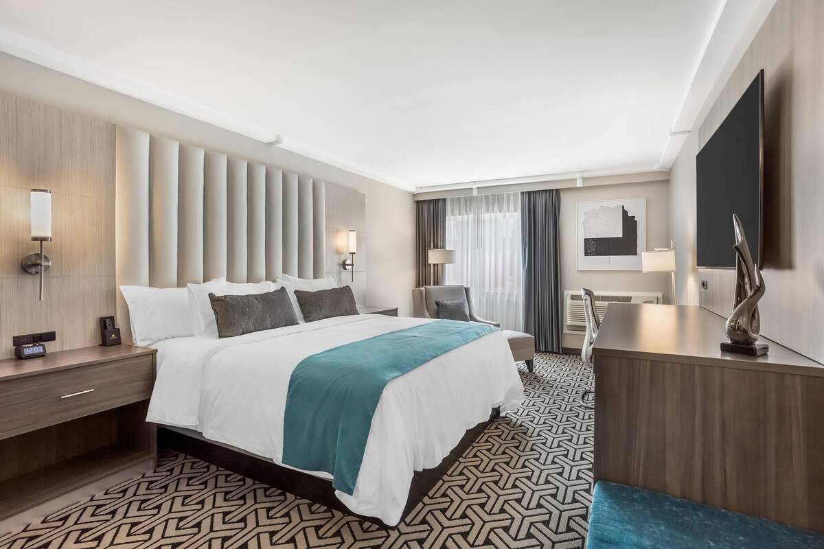 Una habitación de hotel moderna con una cama grande, mesitas de noche, un escritorio y una silla.