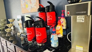 A kitchen area with a coffee station, including multiple coffee makers, a coffee machine, and various condiments.