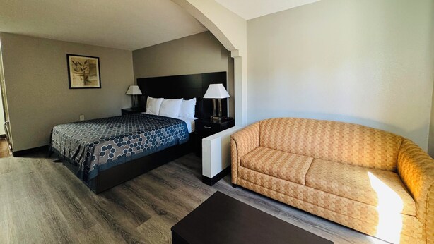 A hotel room with a bed, a sofa, a small table, and a nightstand with lamps.