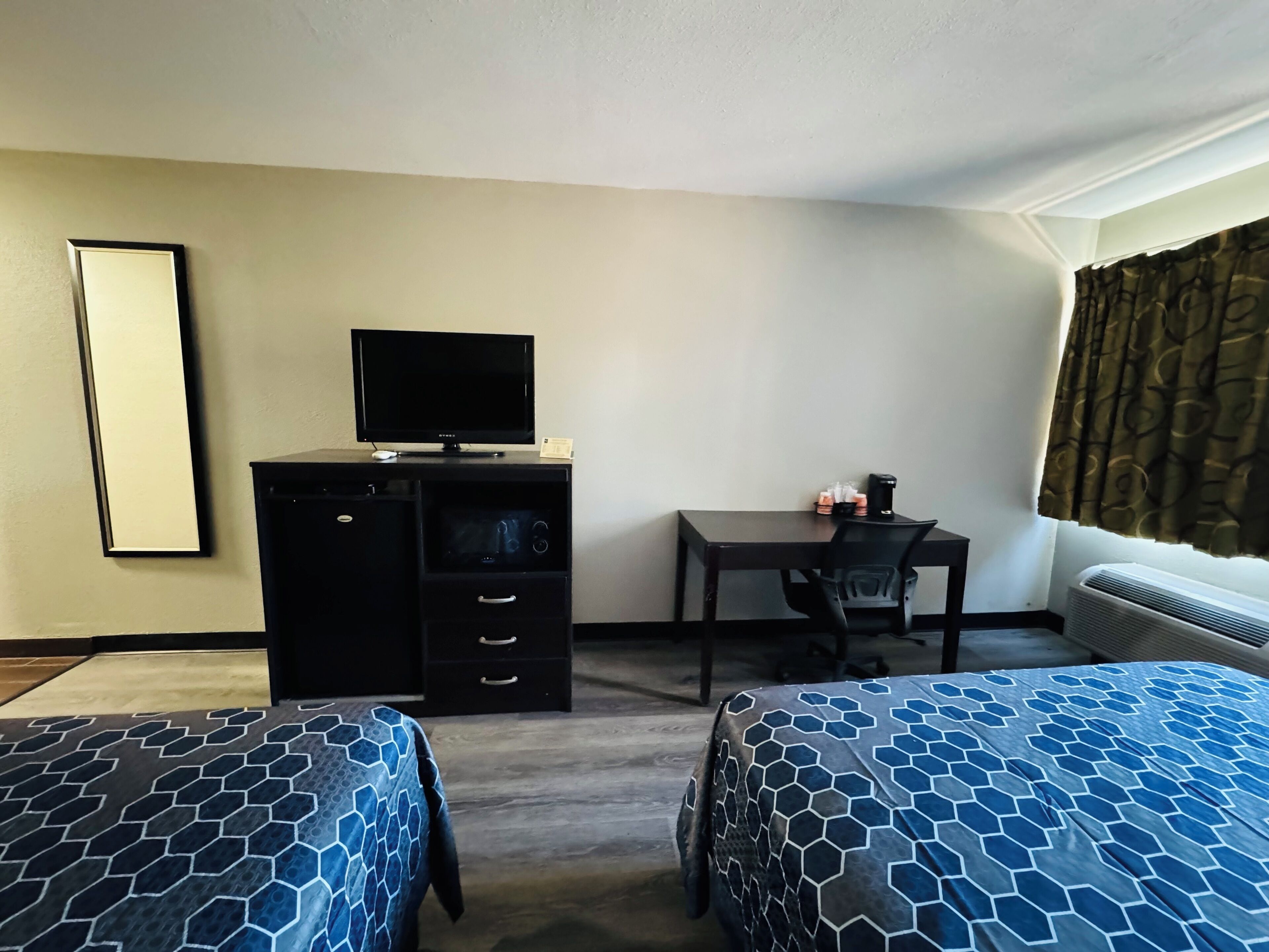 A hotel room with two beds, a desk, a television, and a window with curtains.