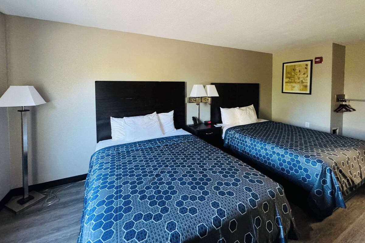Habitación de hotel con dos camas, cada una con cabecero y mesita de noche con lámparas.