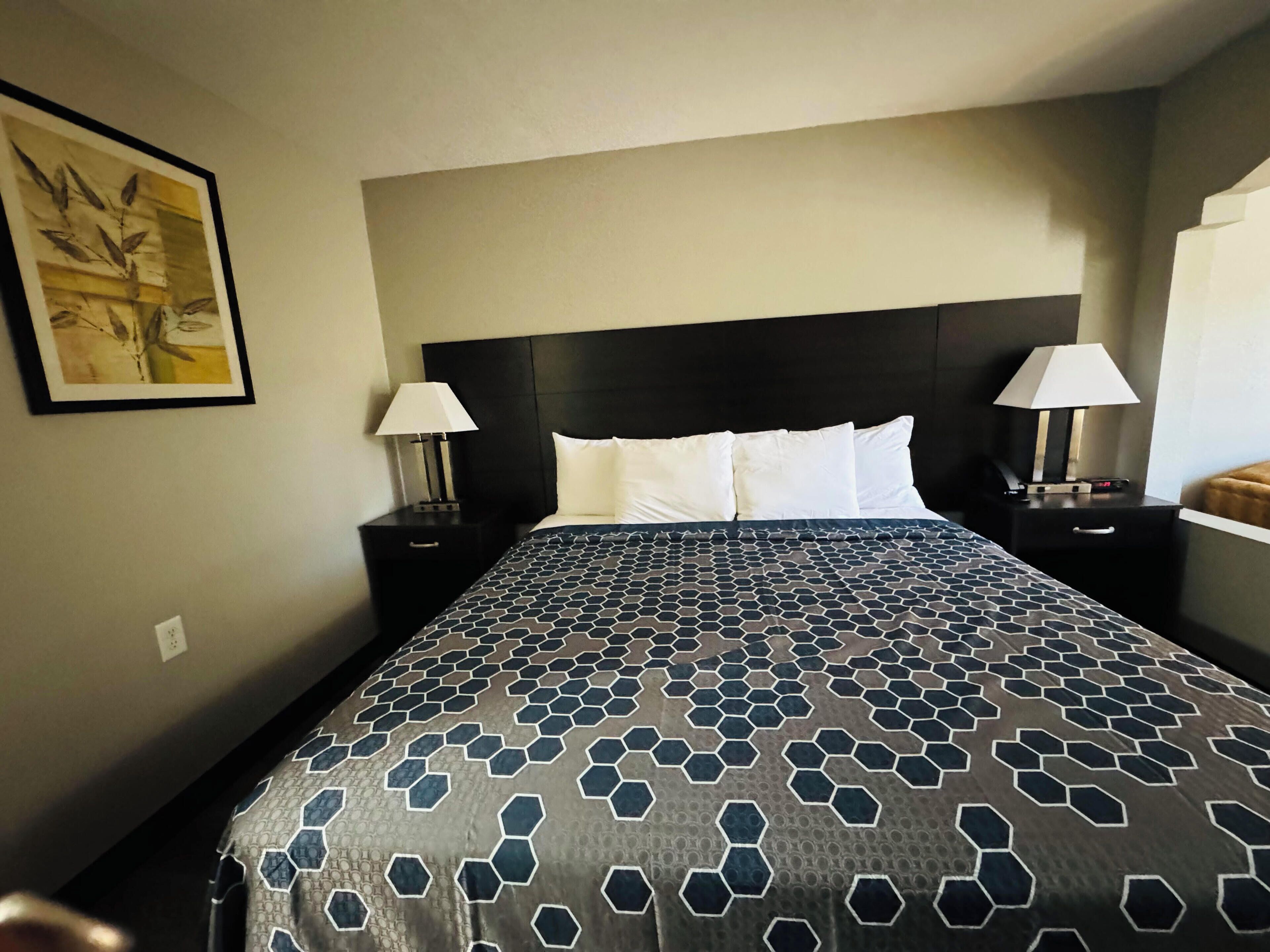 A hotel room with a large bed, two bedside tables with lamps, a headboard, and a framed picture on the wall.
