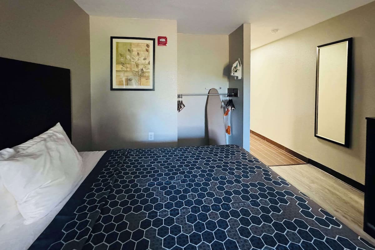 Habitación de hotel con cama, un espejo grande, una obra de arte en la pared y un perchero.