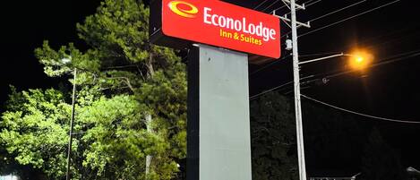 A night-time view of an EconoLodge Inn & Suites sign with a red and yellow logo, surrounded by well-lit trees and a grassy area.