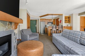 Una sala de estar con chimenea, sofá, sillón y una zona de cocina con refrigerador, microondas y armarios.