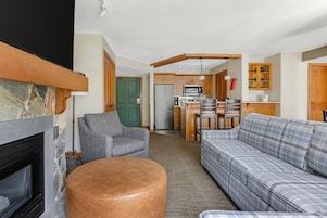 Un salon avec une cheminée, un canapé, un fauteuil et un coin cuisine équipé d’un réfrigérateur, d’un four à micro-ondes et de placards.