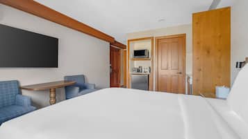 Habitación de hotel con cama, escritorio, televisión de pantalla plana, kitchenette y sofá azul.