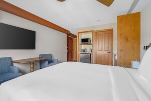 Habitación de hotel con cama, escritorio, televisión de pantalla plana, kitchenette y sofá azul.