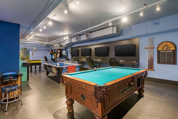 Une table de billard dans une pièce avec un mur bleu, un téléviseur et un tableau d’affichage des scores.