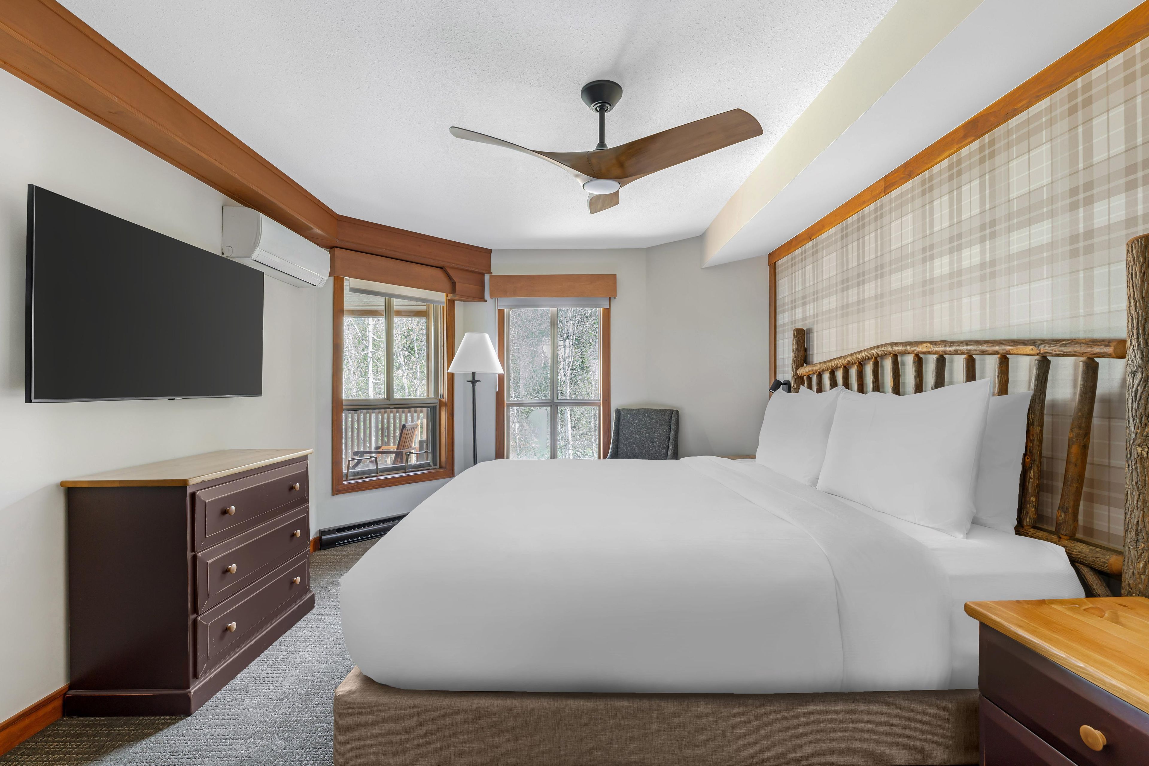 A bedroom with a bed, a dresser, a television, a ceiling fan, and a window with a view.