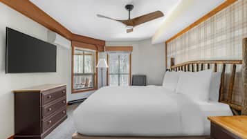A bedroom with a bed, a dresser, a television, a ceiling fan, and a window with a view.