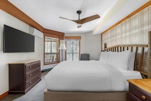 Un dormitorio con cama, cómoda, televisor, ventilador de techo y ventana con vistas.