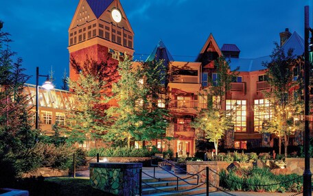 A hotel with a prominent clock tower, multiple balconies, and a well-lit outdoor area with trees and a stone pathway.