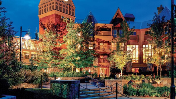 A hotel with a prominent clock tower, multiple balconies, and a well-lit outdoor area with trees and a stone pathway.