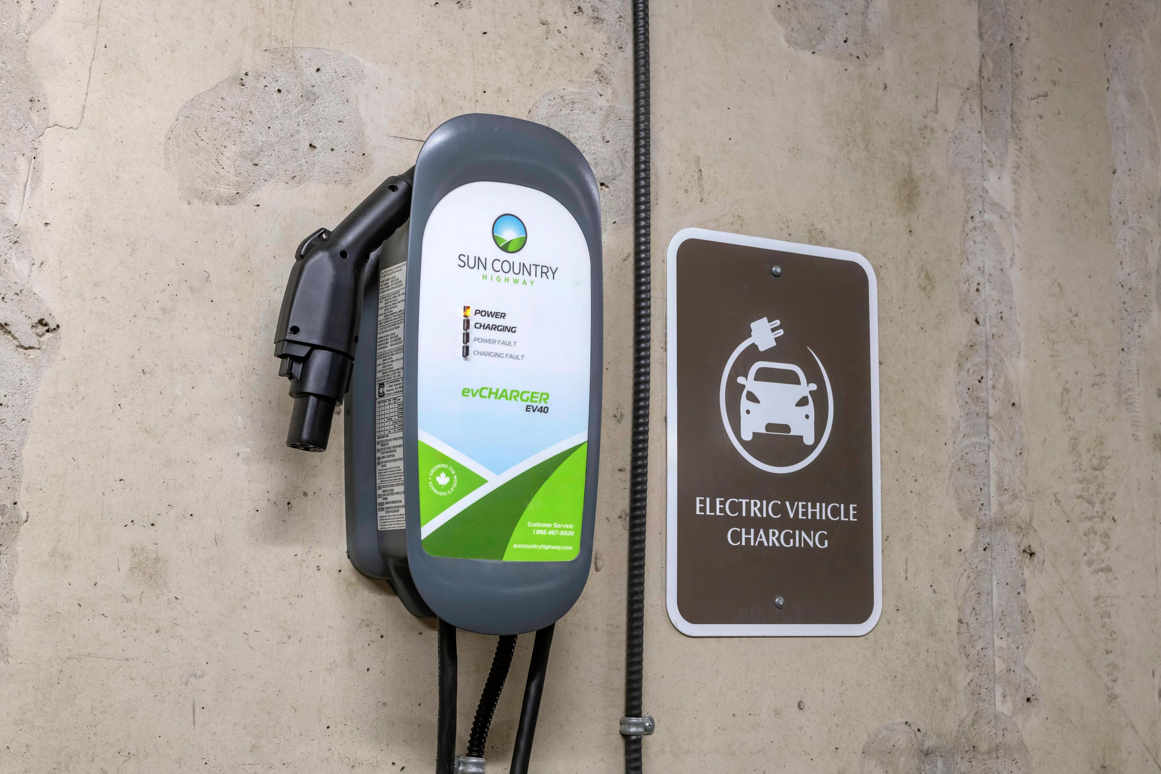 An electric vehicle charging station with a sign indicating 'ELECTRIC VEHICLE CHARGING' and a charging cable connected to a vehicle.