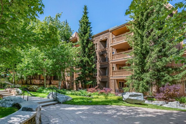 A multi-story building with balconies, surrounded by lush greenery and a stone pathway. - Hilton Grand Vacations Club Whistler (Whistler)