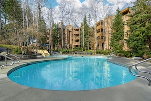A swimming pool surrounded by trees and a building with balconies.