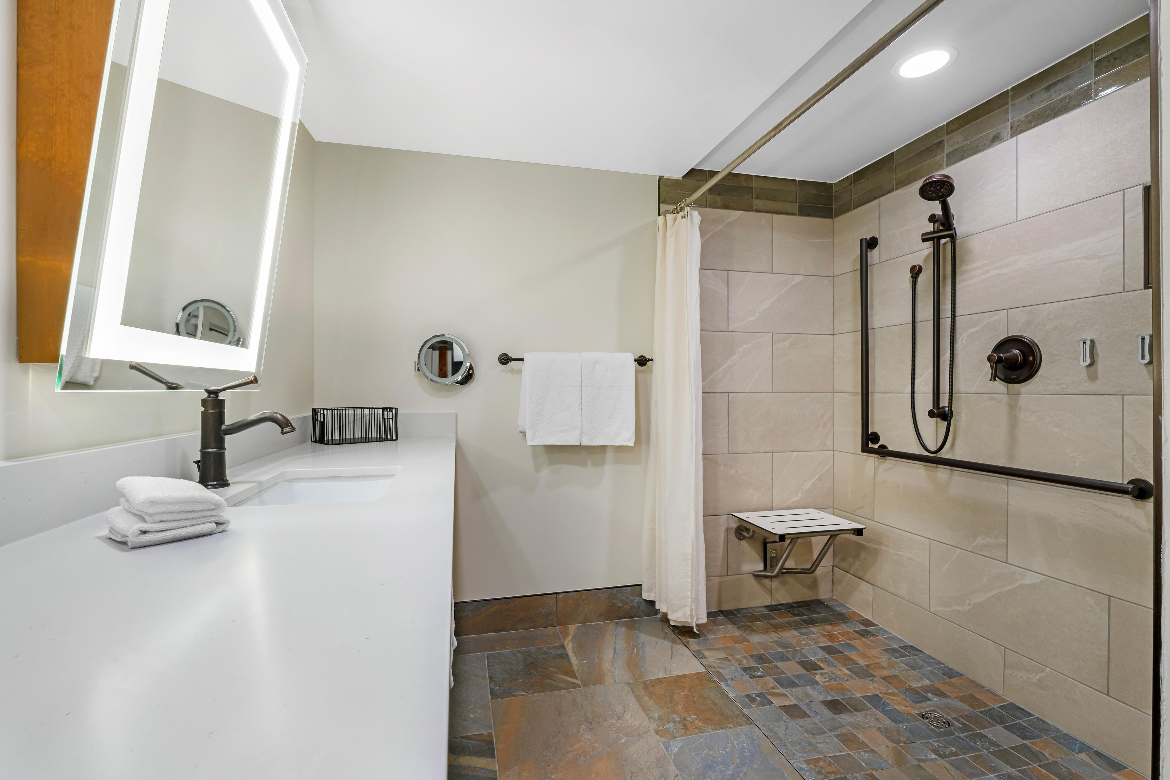 A modern bathroom with a white sink, a mirror, a towel rack, a shower with a handheld showerhead, and a small shelf.