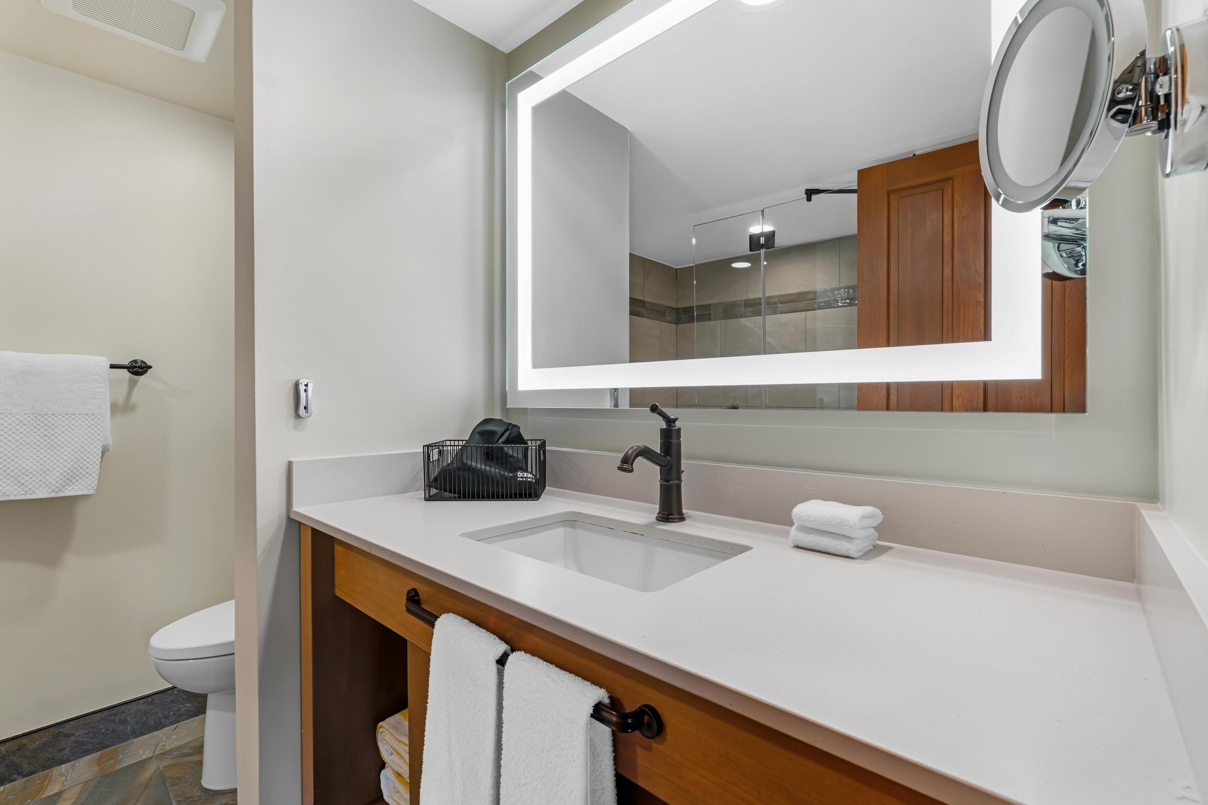 A modern bathroom with a white sink, a large mirror, and a wooden vanity.