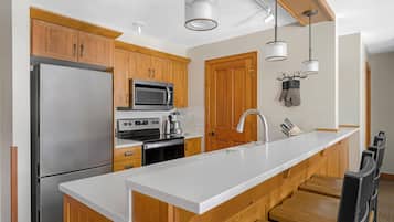 A modern kitchen with wooden cabinets, stainless steel appliances, a white countertop, and pendant lighting.