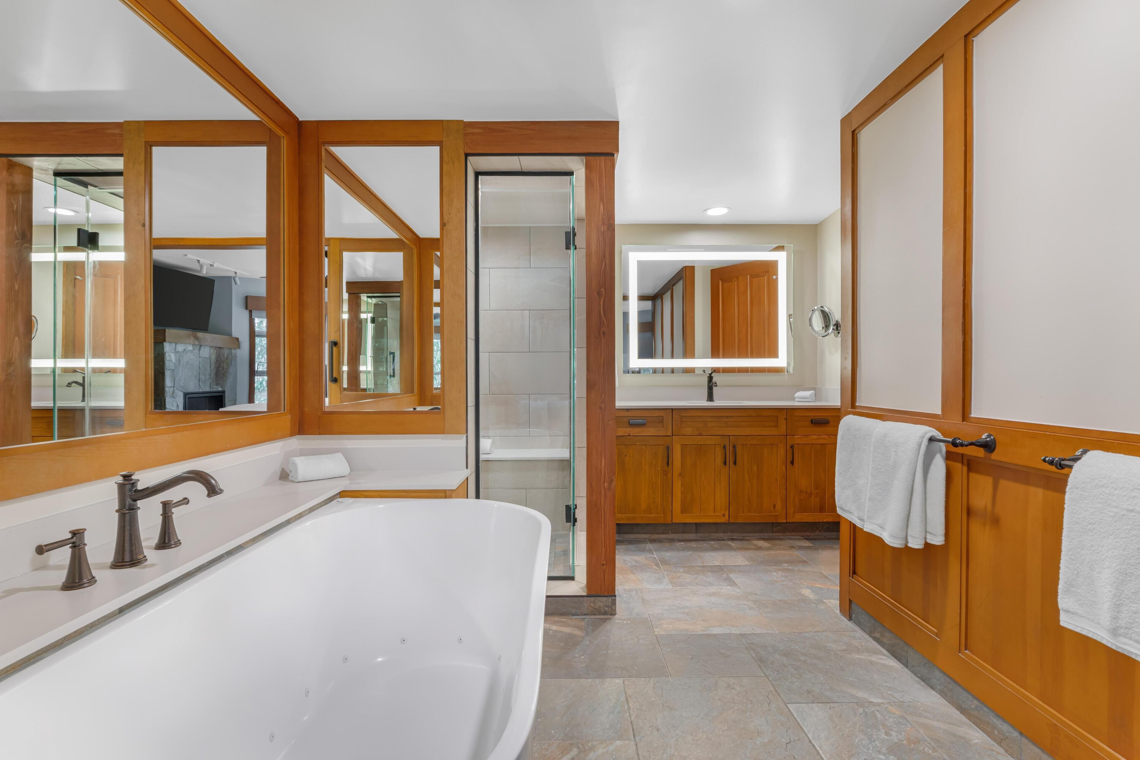 A modern bathroom with a freestanding bathtub, wooden cabinetry, and a large mirror.