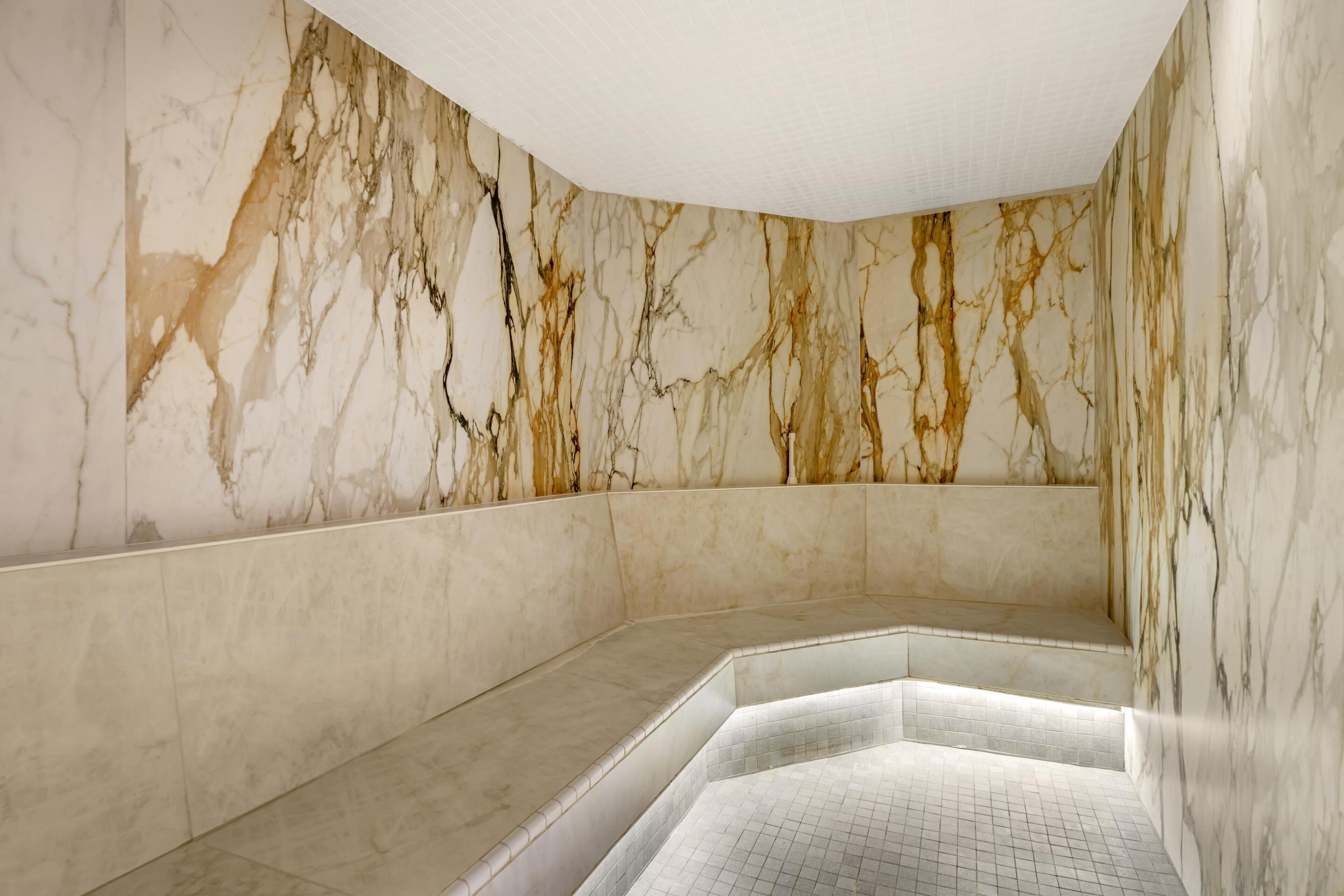 A marble-walled bathroom with a tiled floor and a built-in bench.