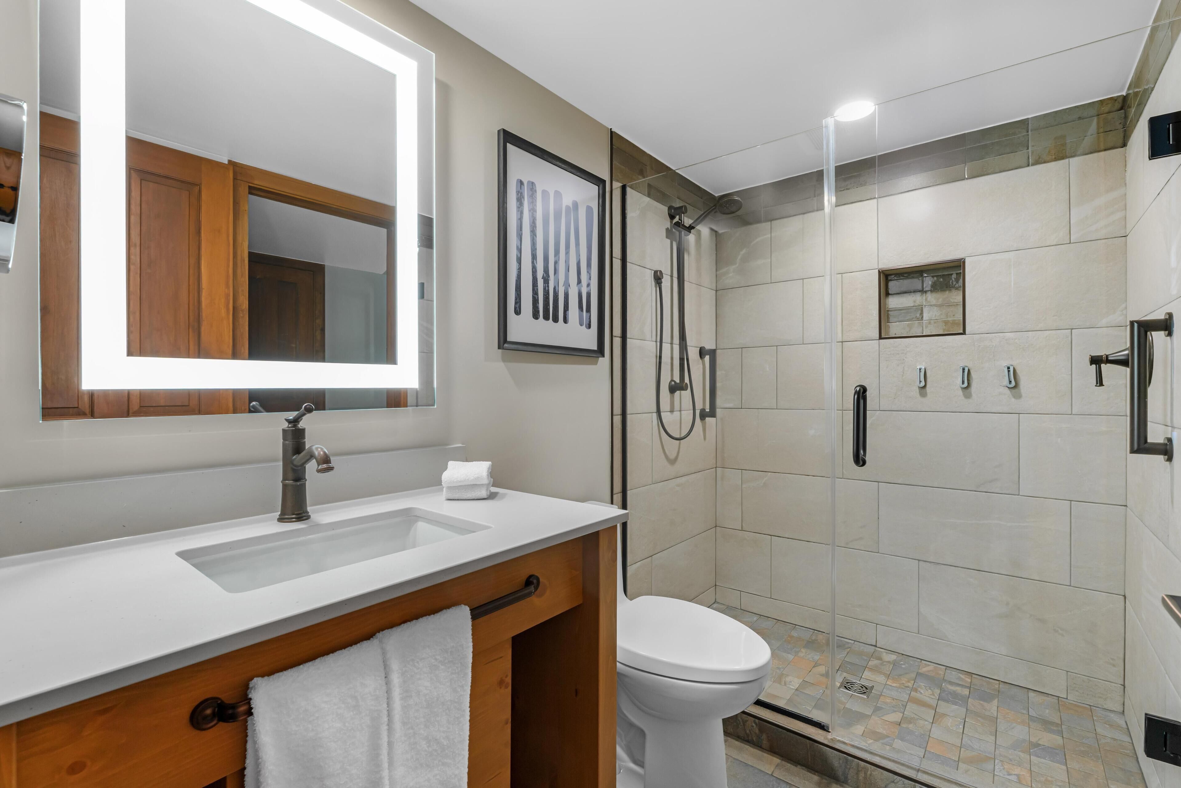 Un baño moderno con un lavabo blanco, un espejo, un inodoro y una zona de ducha.