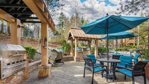 An outdoor patio with stone flooring, a grill, a gazebo, and blue chairs.