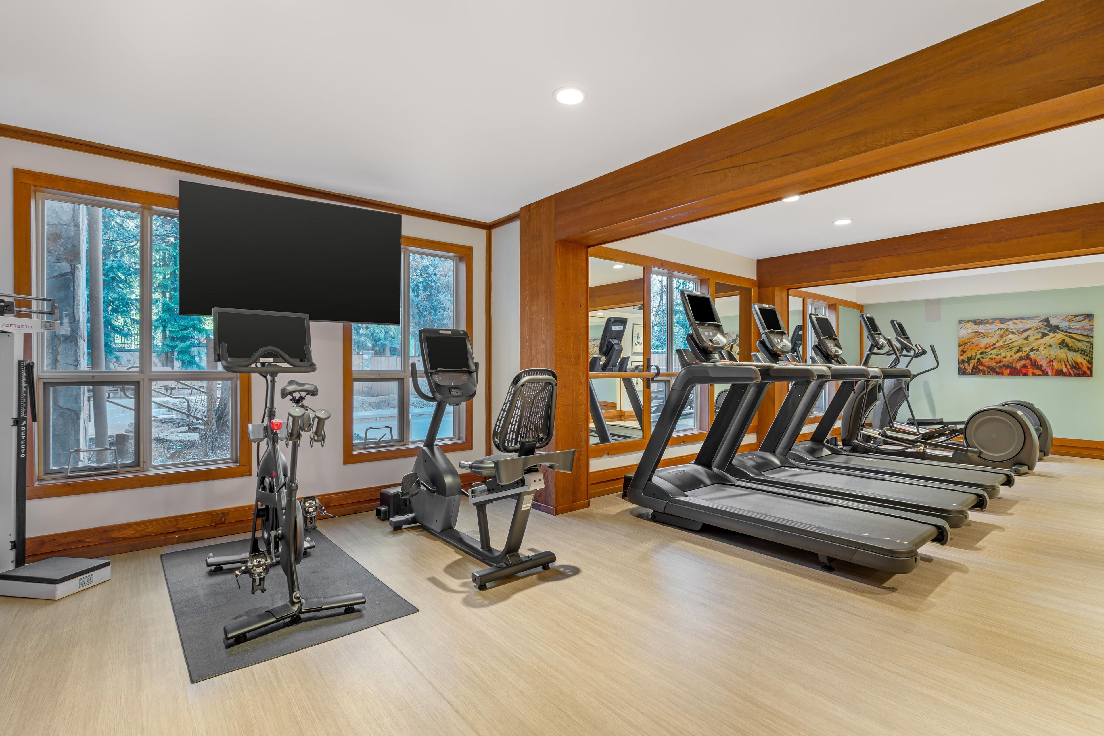 A gym with treadmills, stationary bikes, and a TV screen.