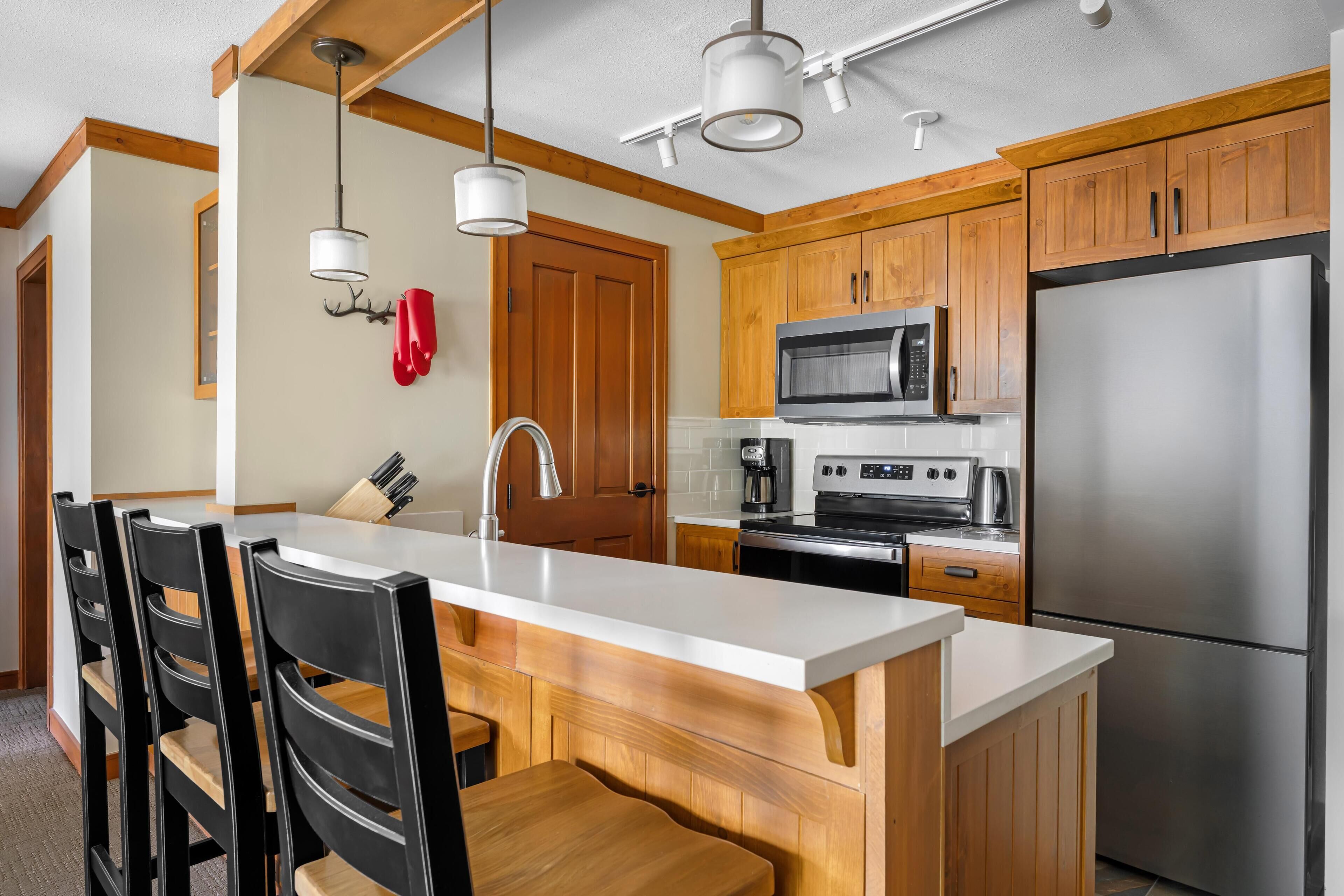 Una cocina moderna con gabinetes de madera, un refrigerador de acero inoxidable, un microondas y una isla grande con taburetes de bar.