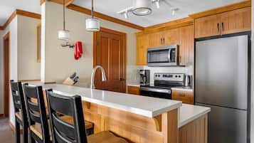 Una cocina moderna con gabinetes de madera, un refrigerador de acero inoxidable, un microondas y una isla grande con taburetes de bar.