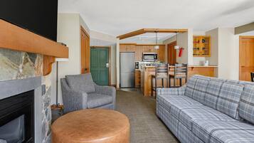 Una sala de estar con chimenea, sofá, sillón y una zona de cocina con refrigerador, microondas y armarios.