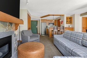 Una sala de estar con chimenea, sofá, sillón y una zona de cocina con refrigerador, microondas y armarios.