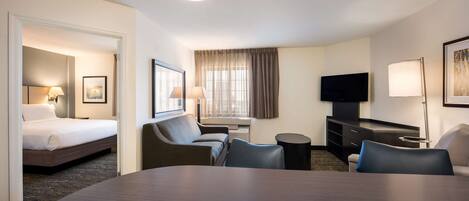 A hotel room with a bed, a desk, two chairs, a TV, and a lamp.