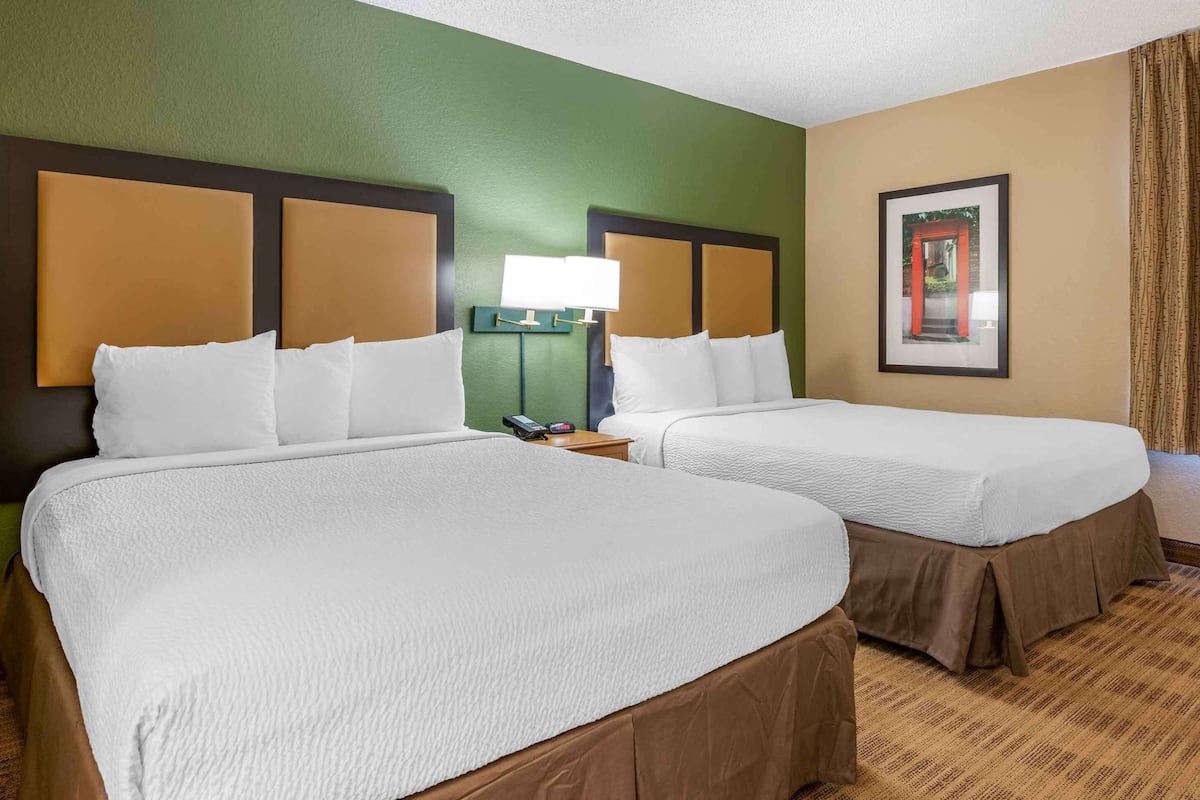 A hotel room with two beds, a nightstand, a lamp, and a framed picture on the wall.